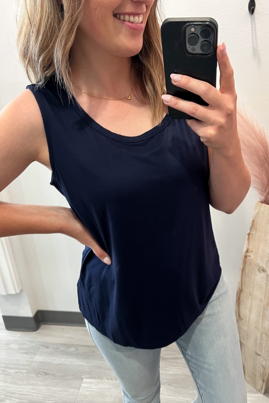 Woman taking a mirror selfie wearing a navy sleeveless top and light blue jeans.