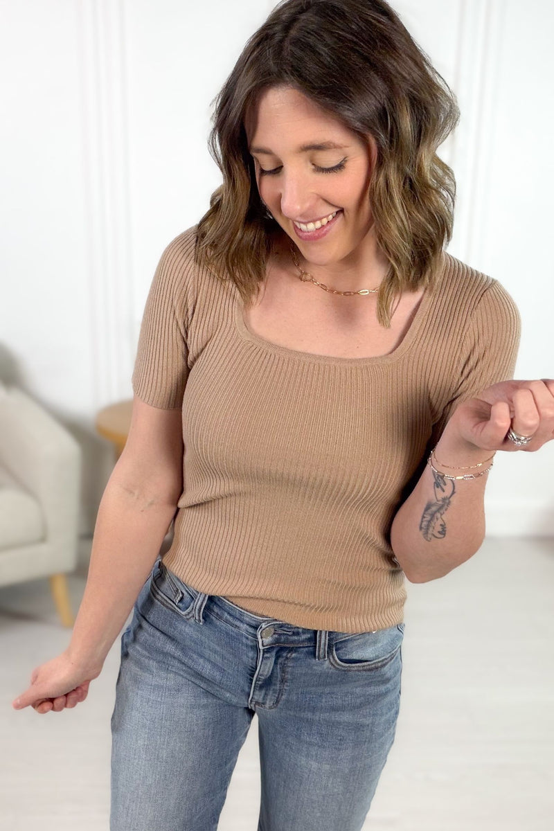 Woman wearing a latte ribbed tee and blue jeans indoors.