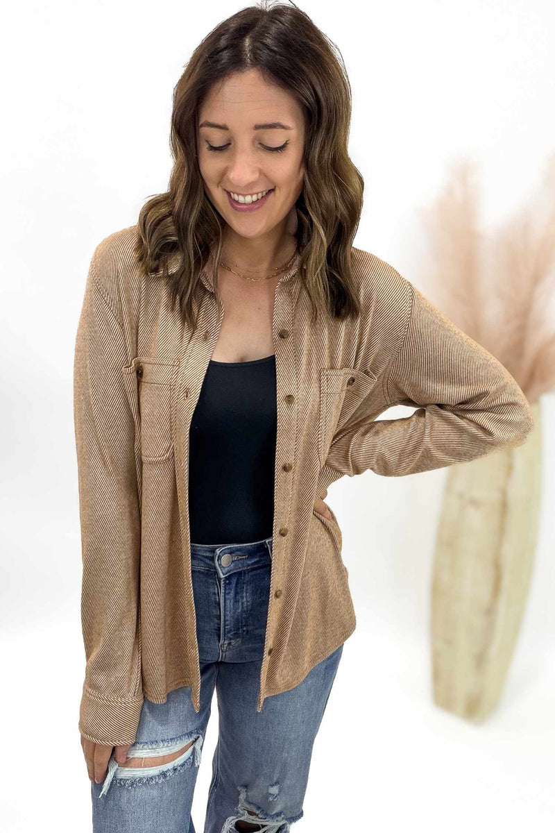 Woman wearing a rust striped button up over a black top and blue jeans on a white background