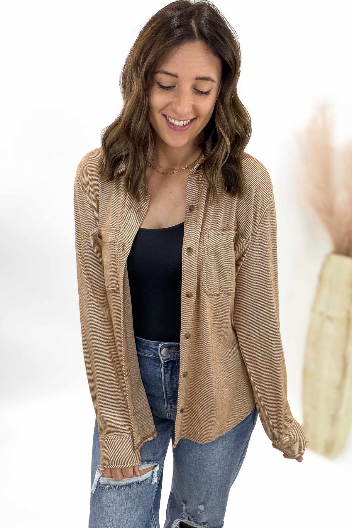 Woman wearing a rust striped button-up shirt over a black top and blue jeans on a white background