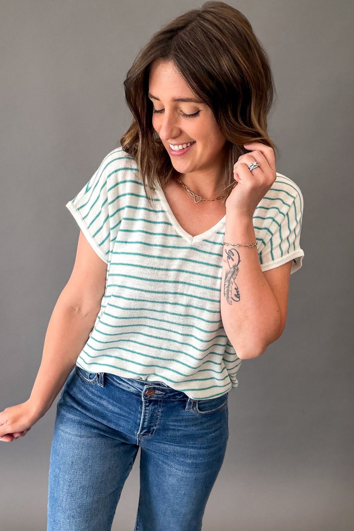 Woman wearing a teal striped shirt and jeans against a gray background