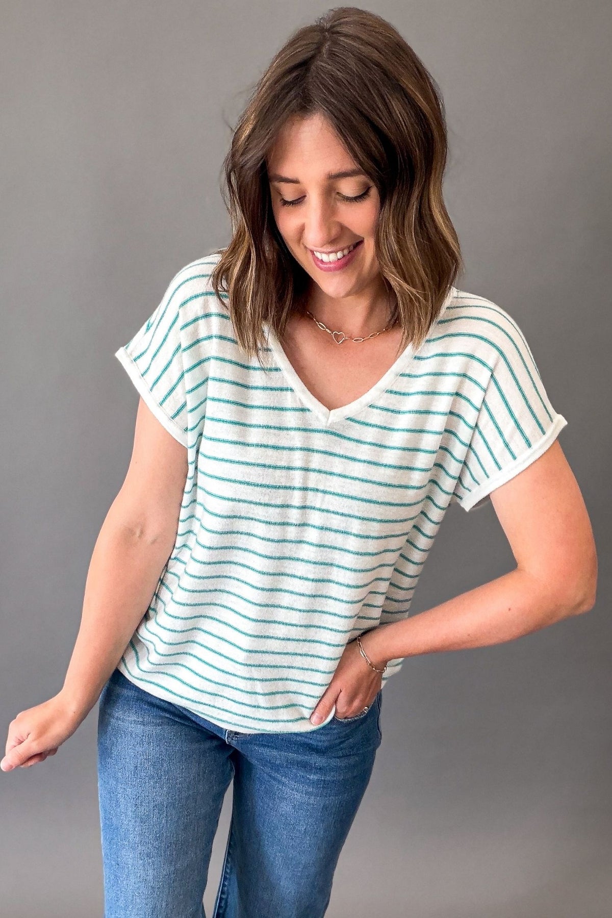 Woman wearing a white t-shirt with teal stripes and blue jeans on a gray background