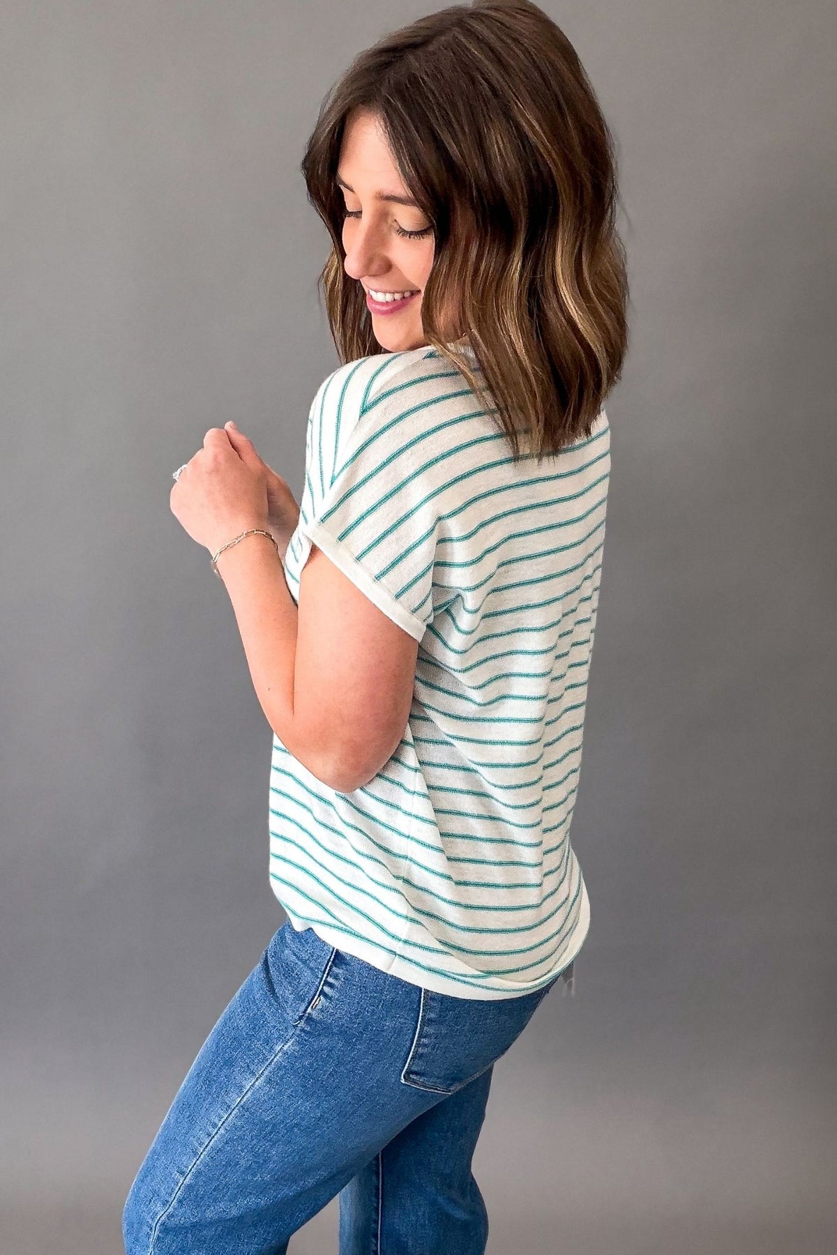 Woman wearing a teal striped shirt and jeans against a gray background
