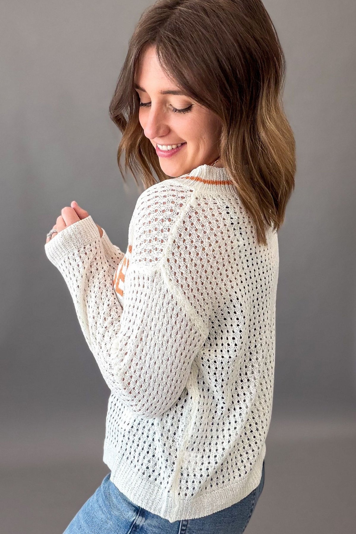 Woman wearing a ivory knit sweater against a gray background