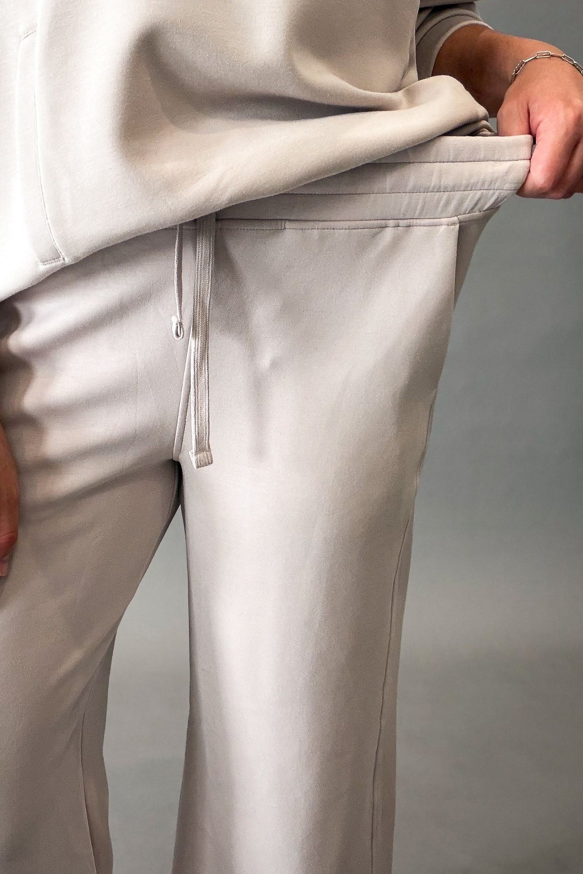Close-up of a person wearing a mocha cream wide-leg sweatpants, pulling the waistband slightly outward with one hand.