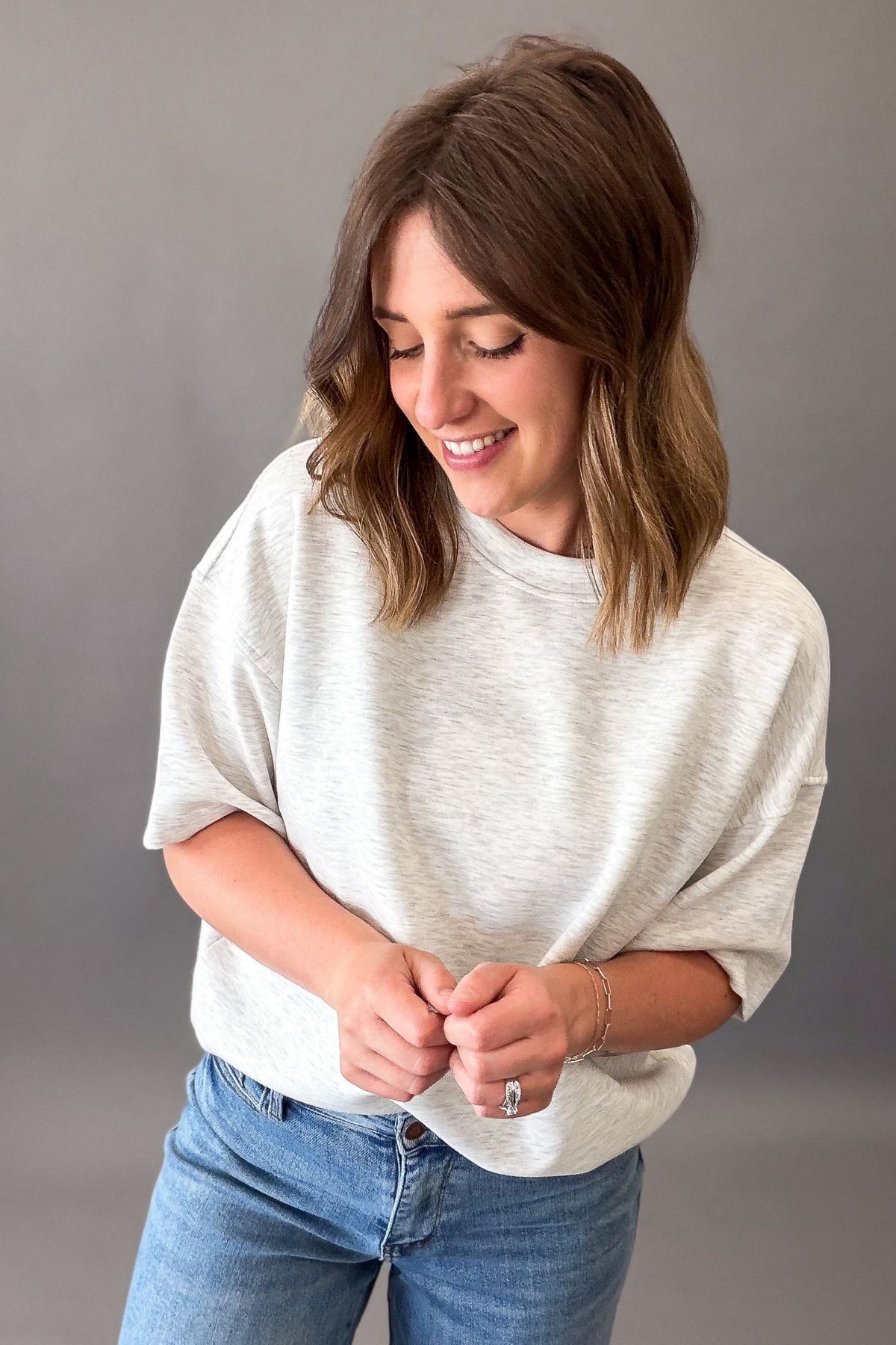 woman wearing a light grey lounge short sleeve top with blue jeans on a grey background