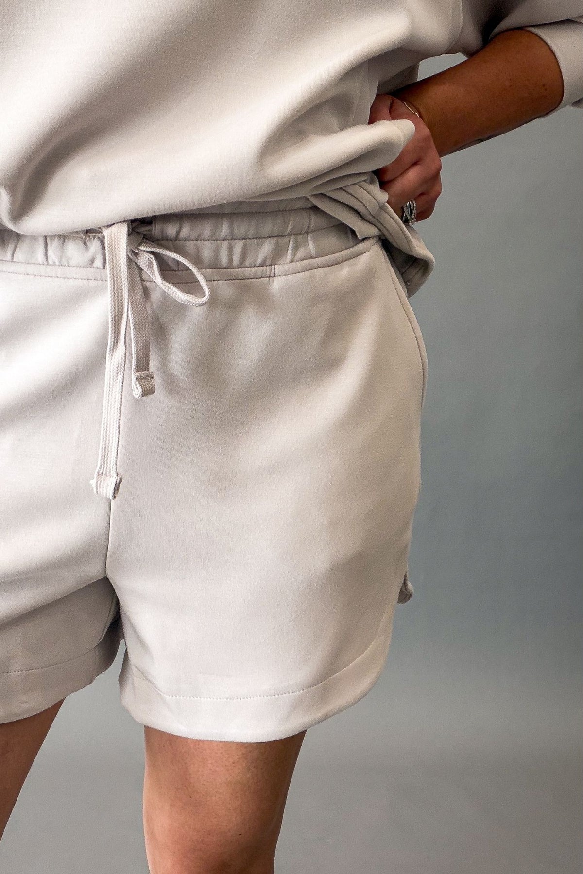 A close-up of a person wearing light mocha cream drawstring shorts and a matching sweatshirt, with the shorts being the primary product shown.