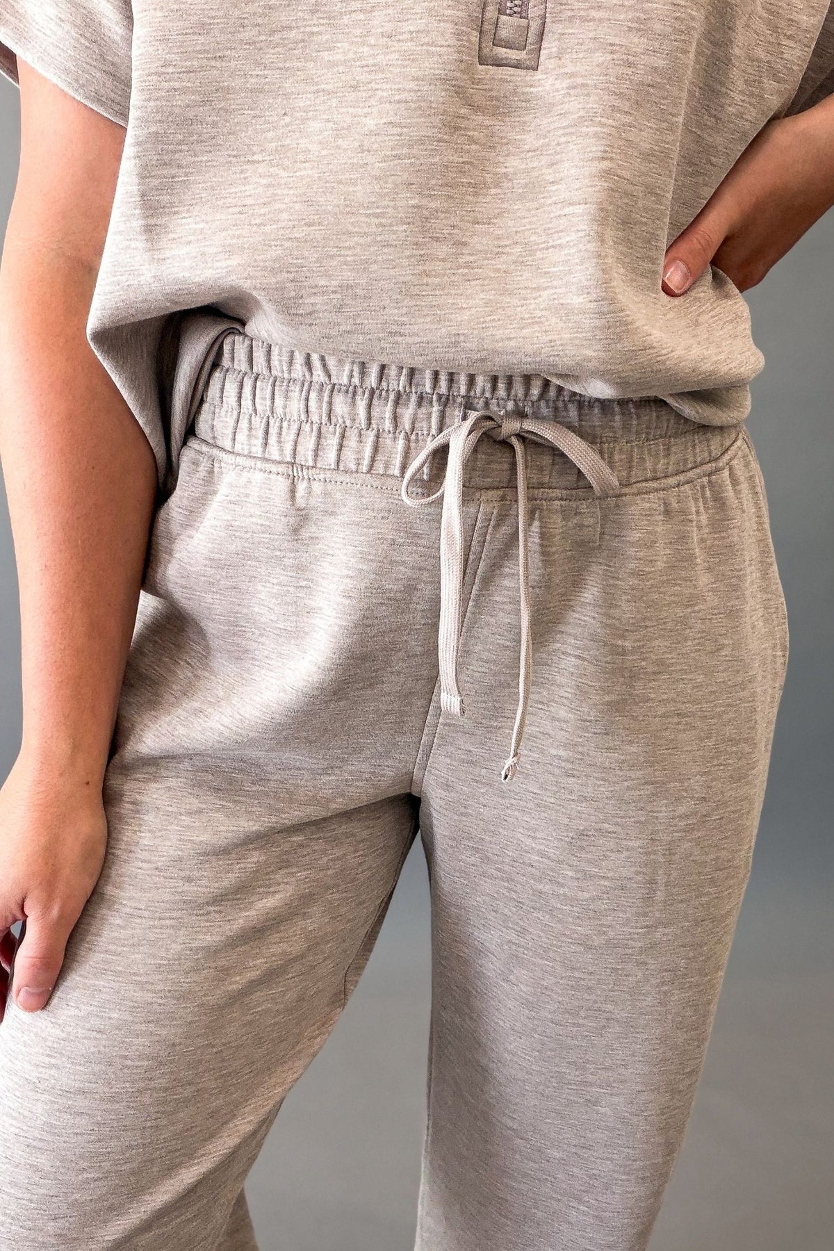 Close-up of a person wearing light heather taupe sweatpants with an elastic waistband and drawstring, paired with a matching heather gray top.