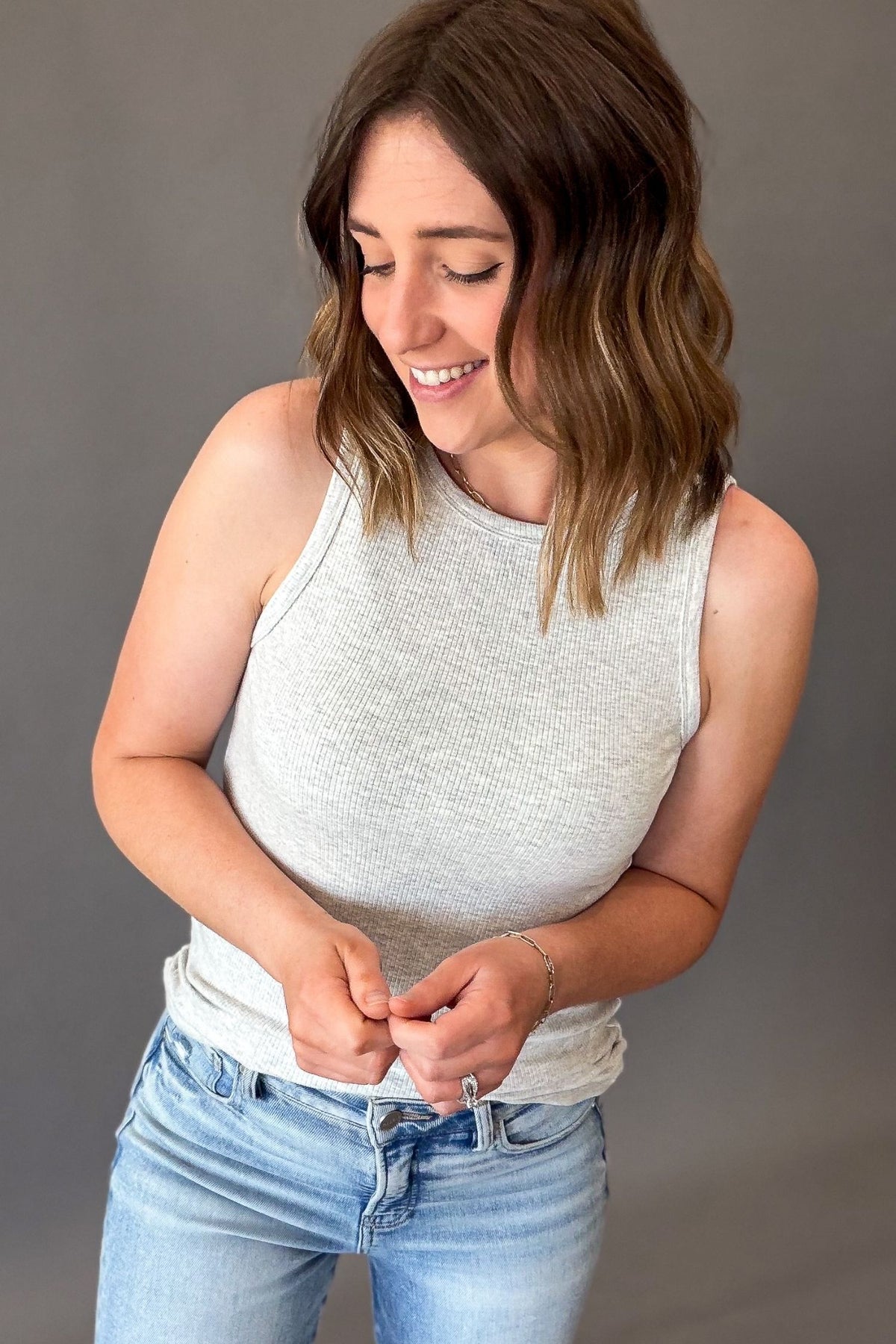 woman wearing a lightweight grey tank tucked in with blue jeans on a grey background