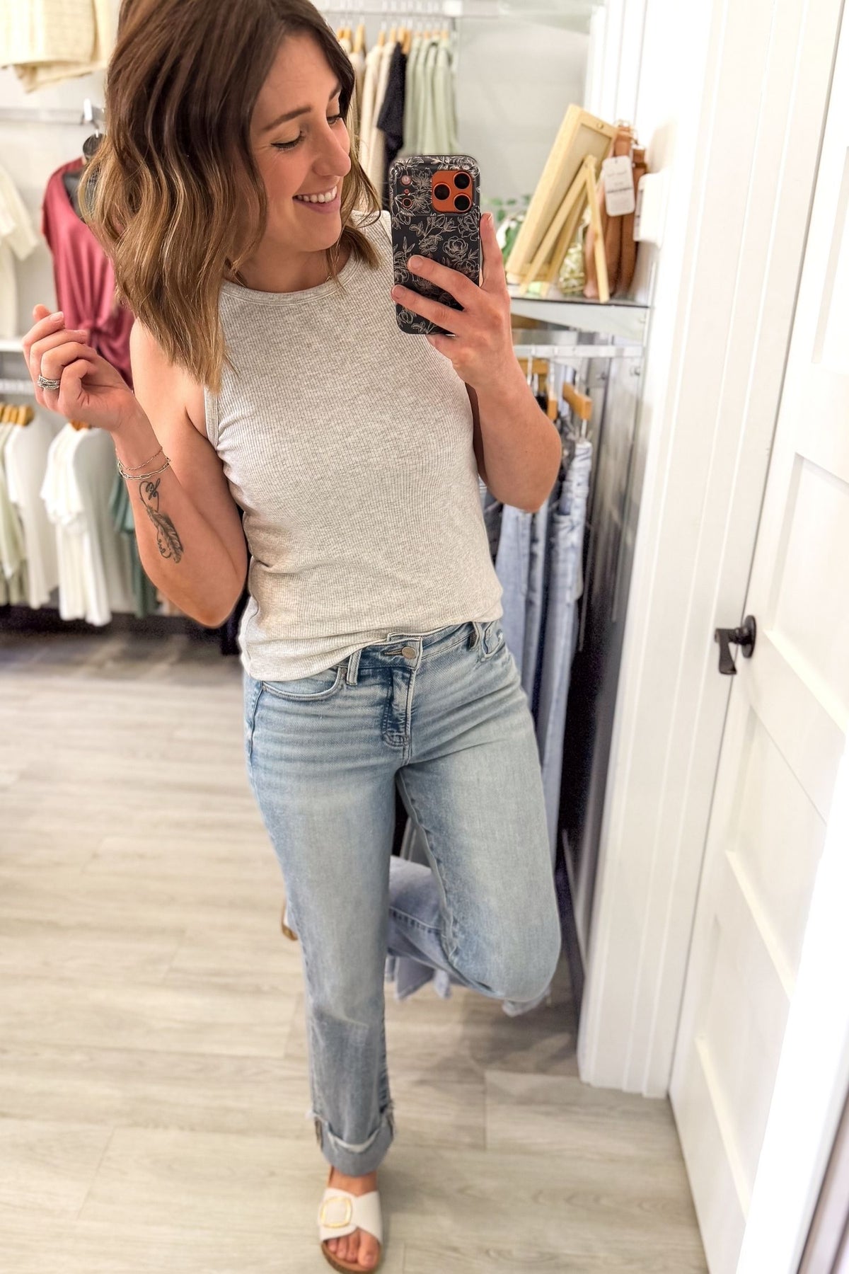 woman taking a mirror selfie wearing a fitted heather grey tank with blue jeans and white sandals in a boutique