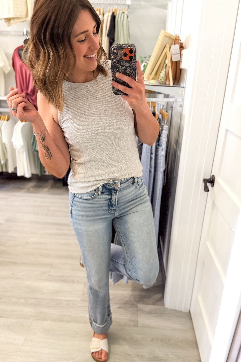 woman taking a mirror selfie wearing a fitted heather grey tank with blue jeans and white sandals in a boutique