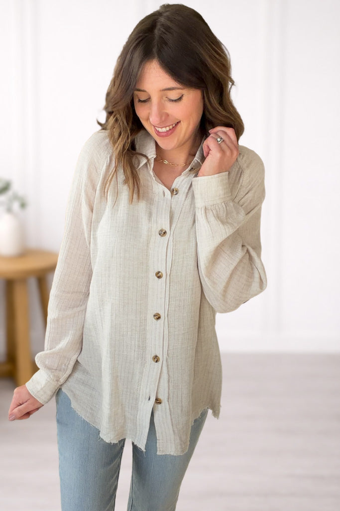 Woman wearing a light-colored button-up shirt and jeans indoors.