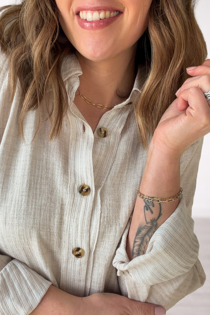 Woman wearing a light-colored shirt with rolled-up sleeves, smiling.