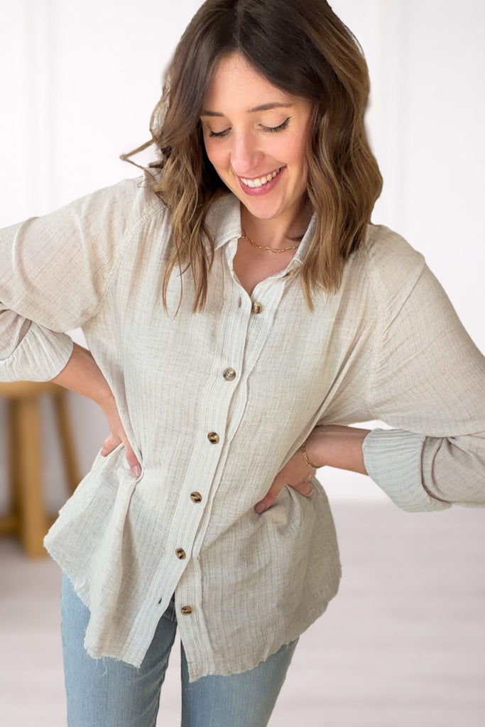 Woman wearing a beige button-up shirt and light blue jeans against a white background