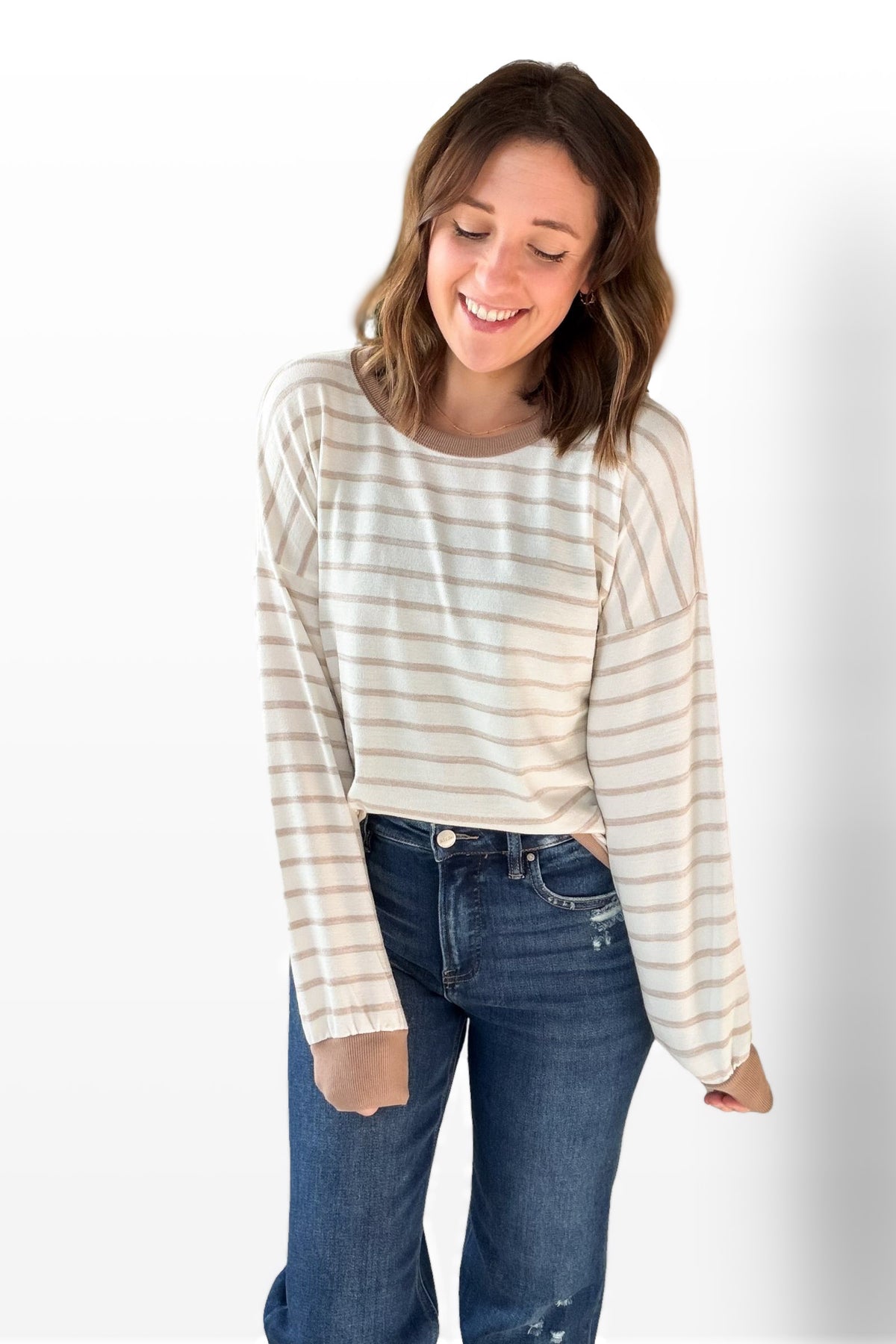 Woman wearing a striped long-sleeve top and blue jeans on a white background