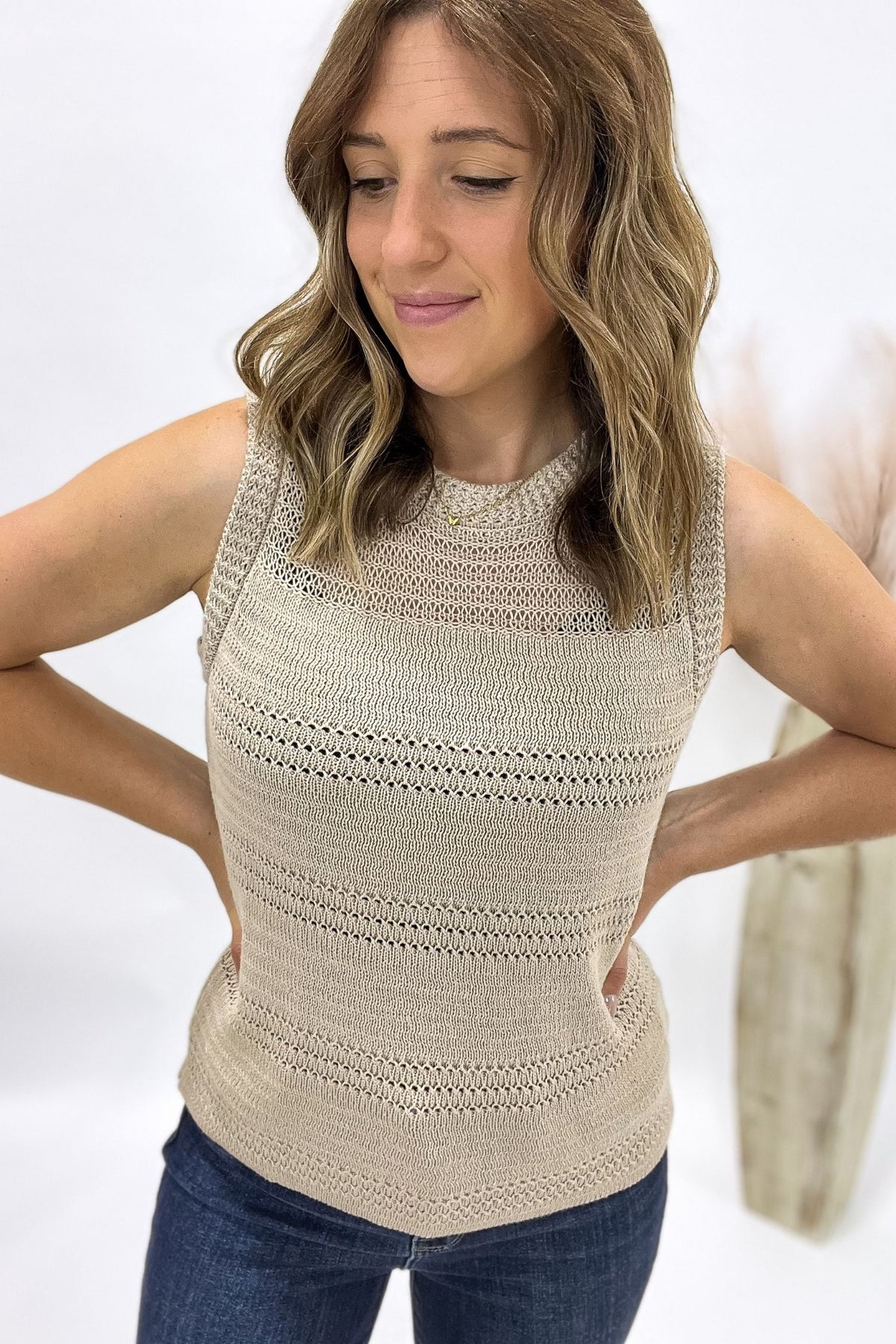 Woman wearing a beige sleeveless crochet top against a white background