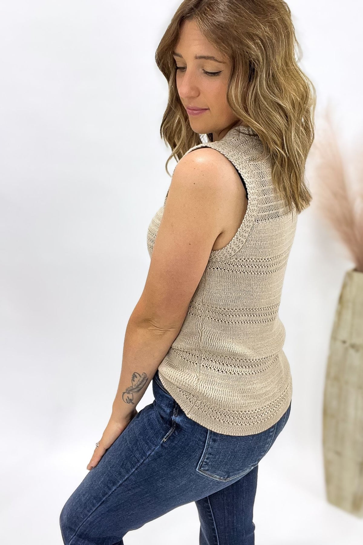 Woman wearing a beige sleeveless knitted top and blue jeans on a white background