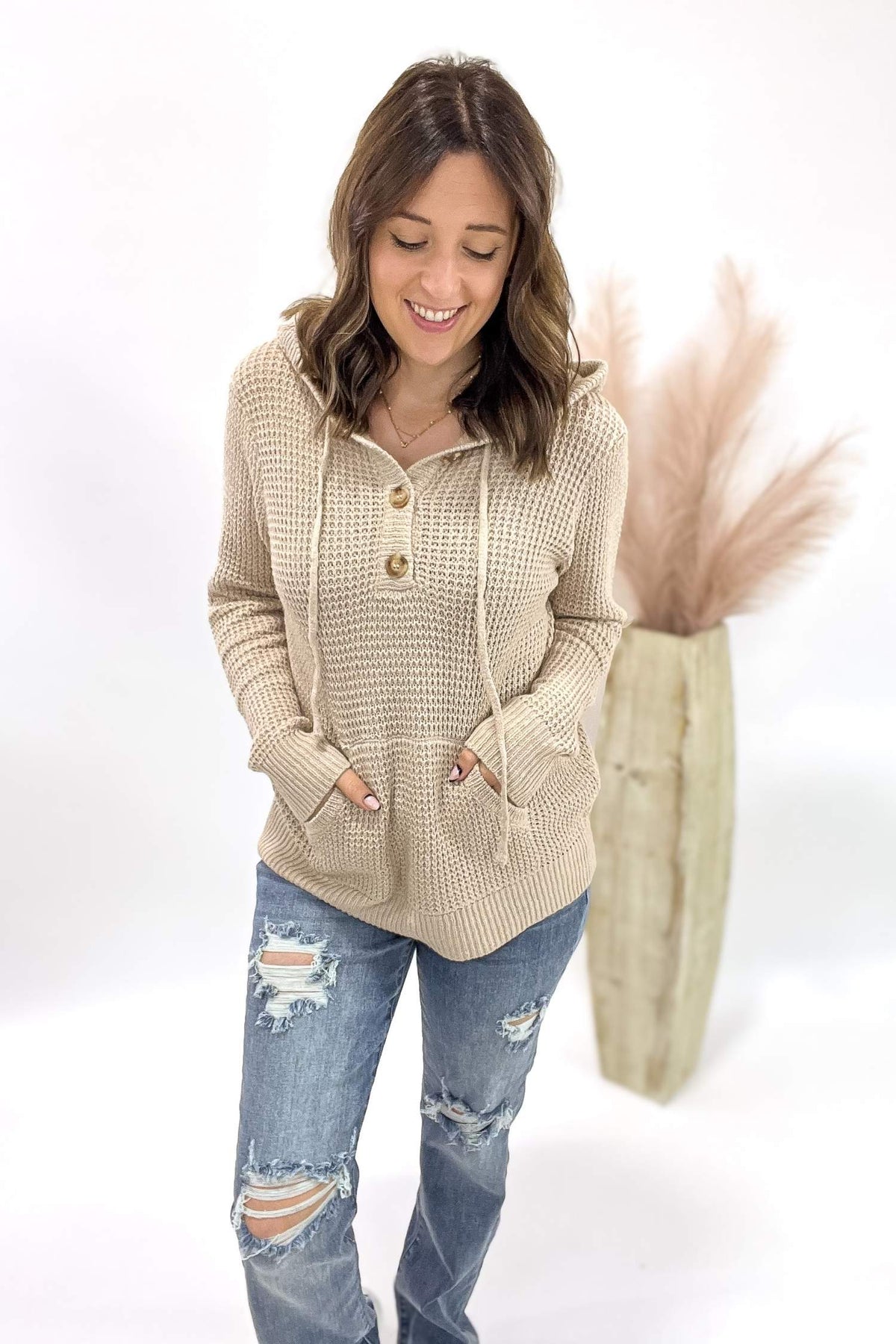 Woman wearing a beige hooded sweater and ripped jeans on a white background
