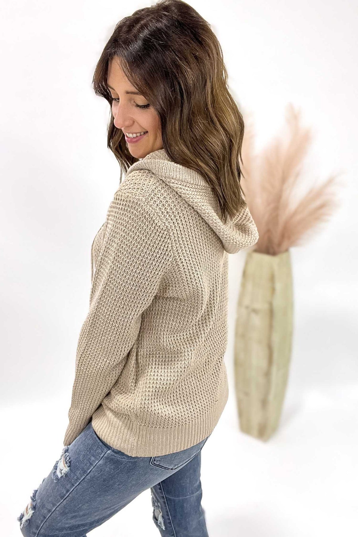 Woman wearing a beige knitted hoodie and jeans on a white background