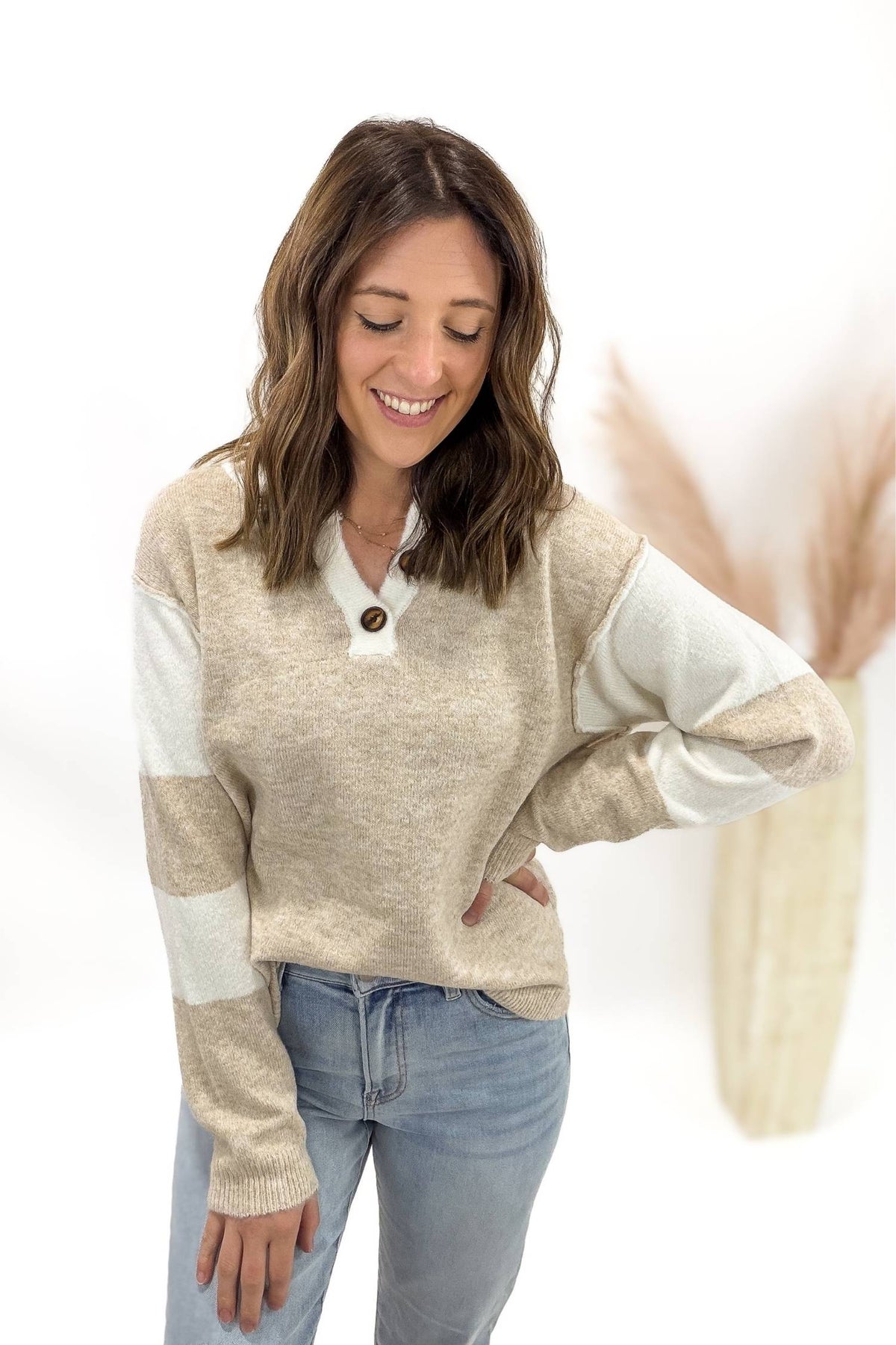 Woman wearing a beige sweater with white sleeves and blue jeans on a white background
