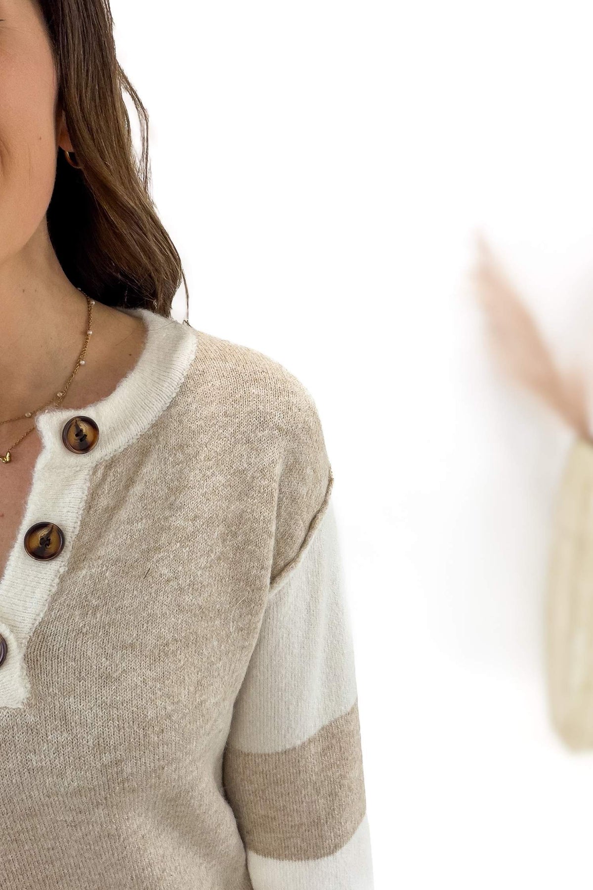 Close-up of a person wearing a beige and white sweater with button details on a white background
