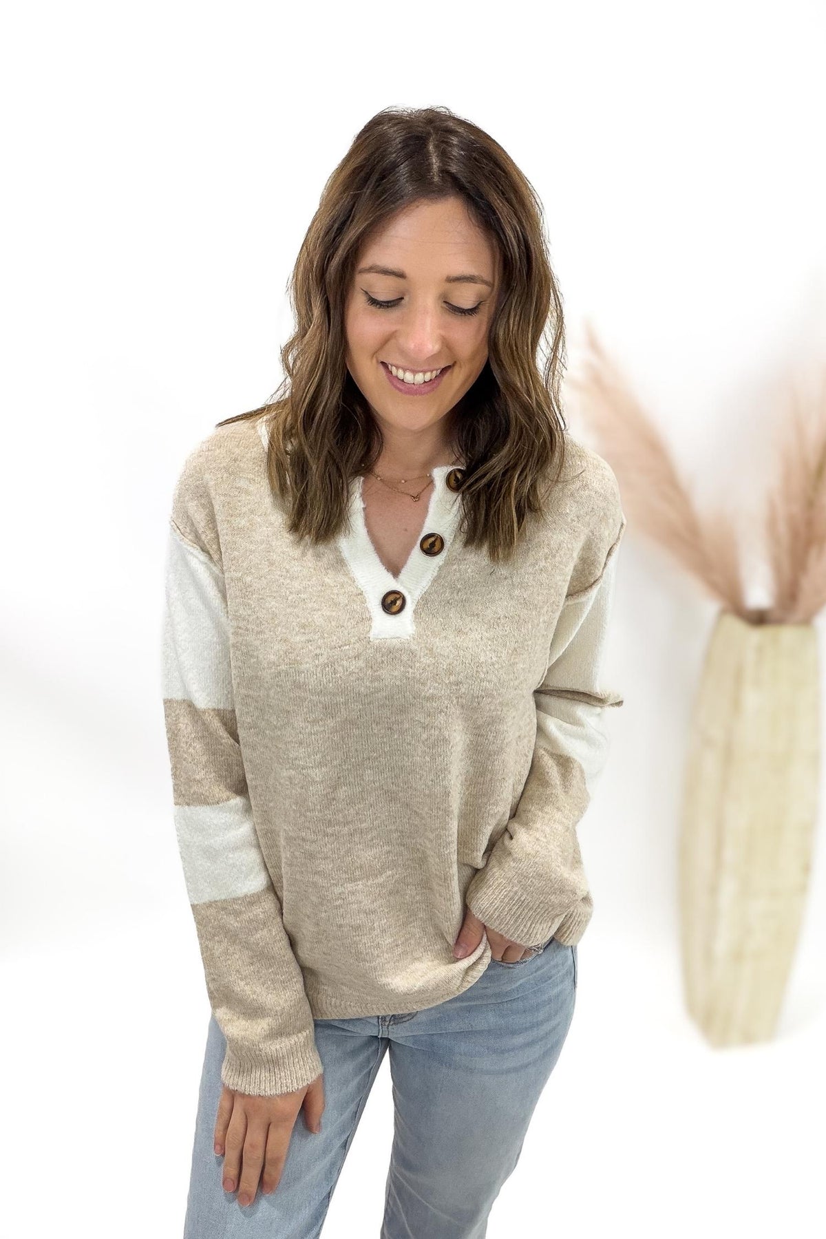 Woman wearing a beige and white long-sleeve top with buttons on a white background