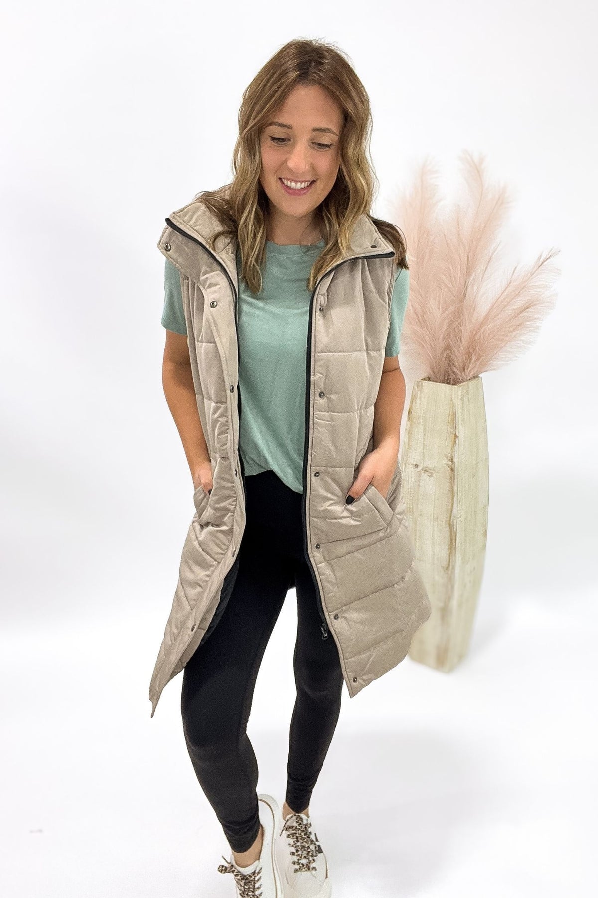 Woman wearing a long beige puffer vest on a white background