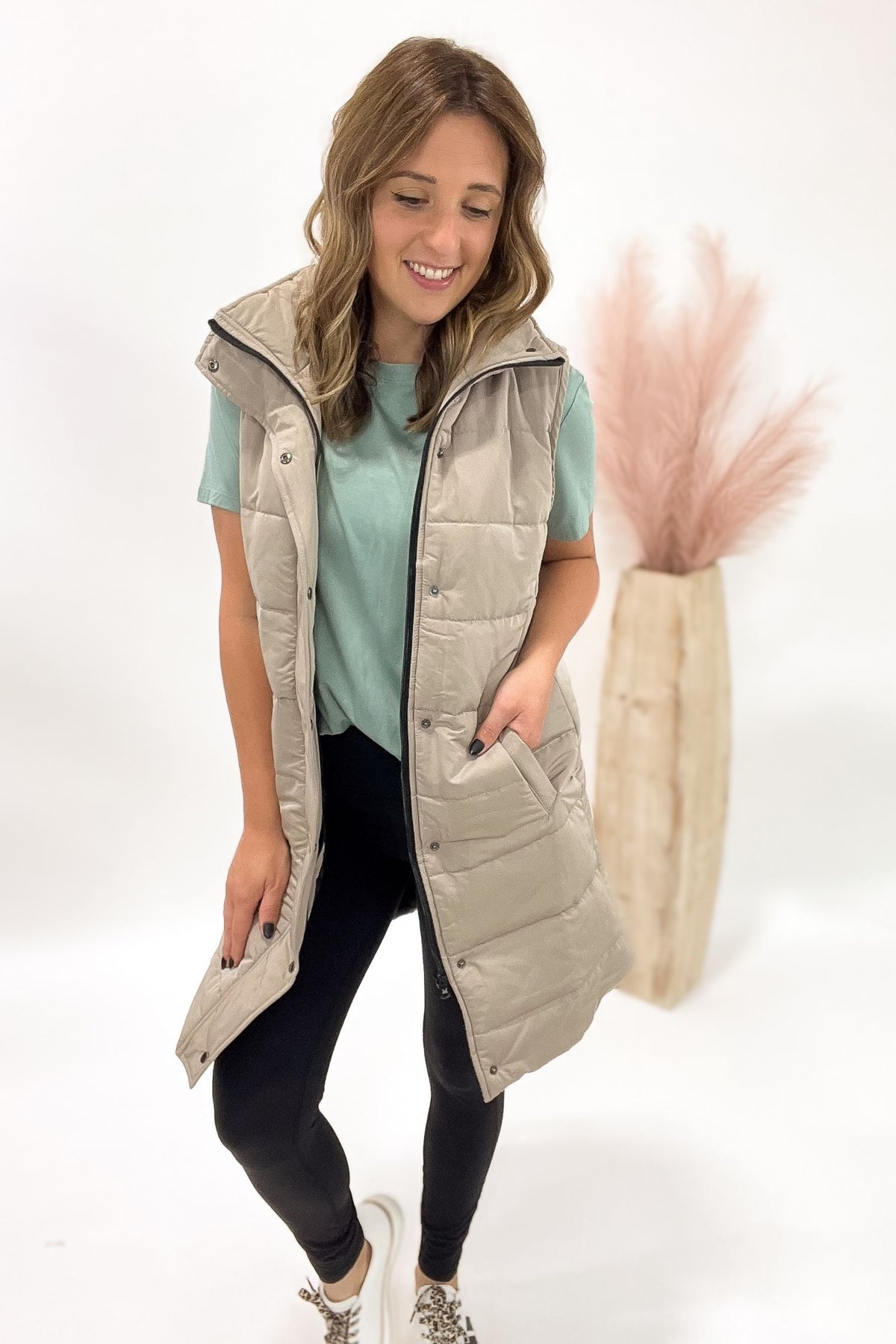 Woman wearing a beige puffer vest over a light blue shirt on a white background