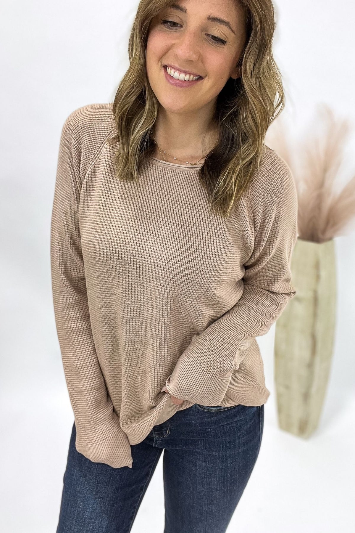 Woman wearing a beige sweater and blue jeans against a white background