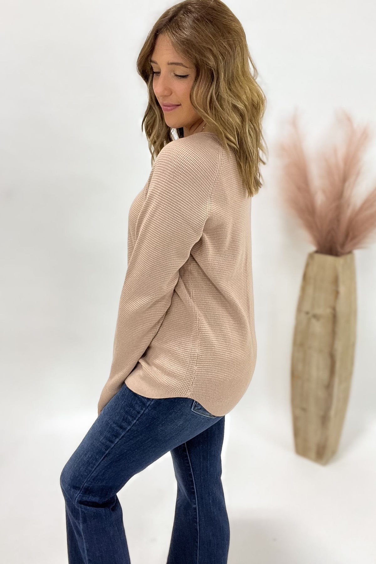 Woman wearing a beige sweater and blue jeans against a white background with decorative elements.