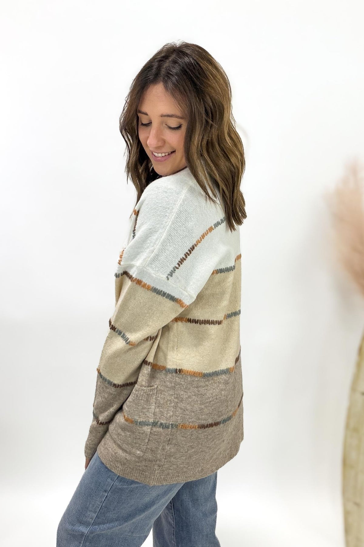 Woman wearing a patterned cardigan and jeans on a white background