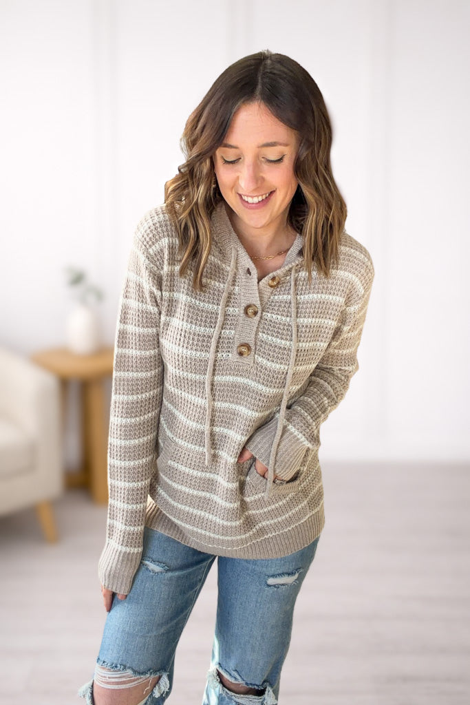 Woman wearing a taupe striped sweater hoodie and jeans indoors with a neutral background