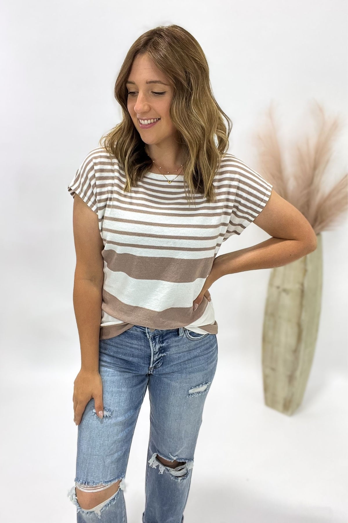Woman wearing a striped shirt and ripped jeans against a white background