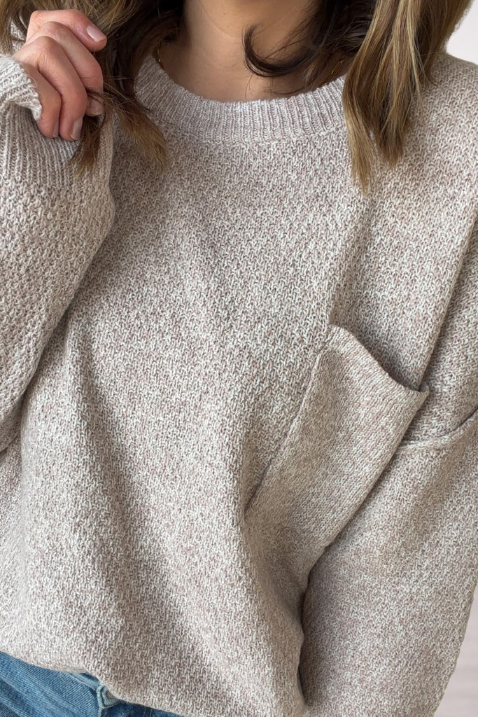 Close-up of a person wearing a taupe knitted sweater with a pocket.