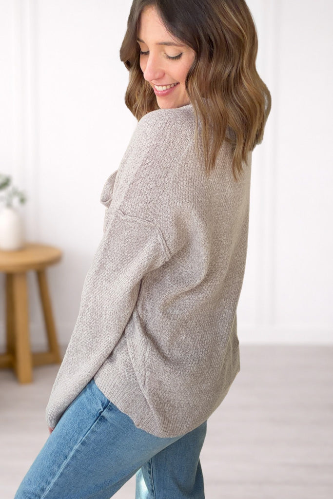 Woman wearing a taupe sweater and blue jeans in a minimal indoor setting