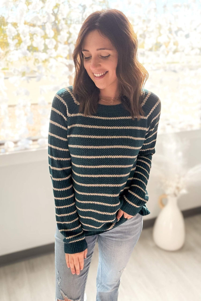 Woman wearing a striped sweater in a bright room with a vase in the background