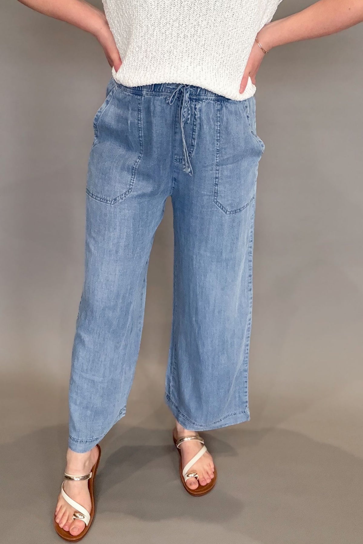 Woman wearing a blue tencel wide leg pant with a white top and sandals