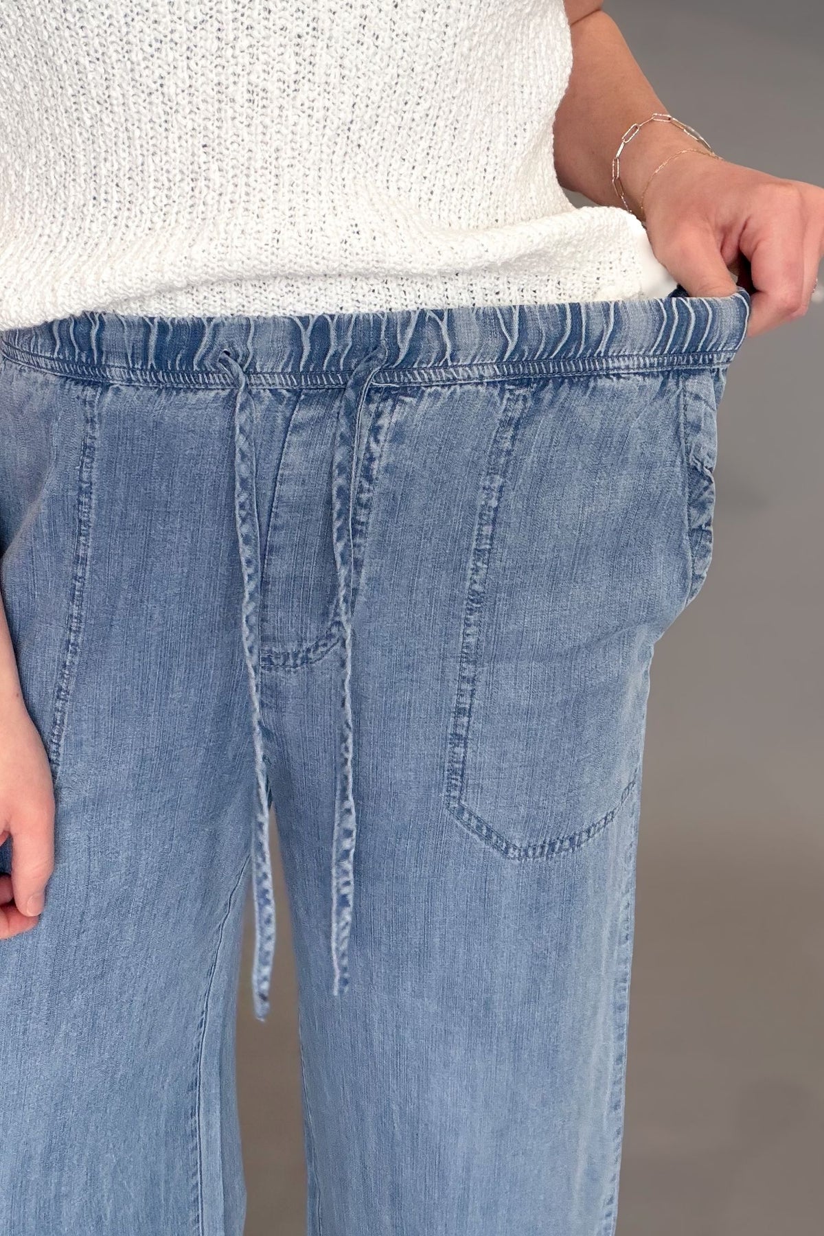 Woman wearing a blue tencel wide leg pant with a white top and sandals showing the elastic band
