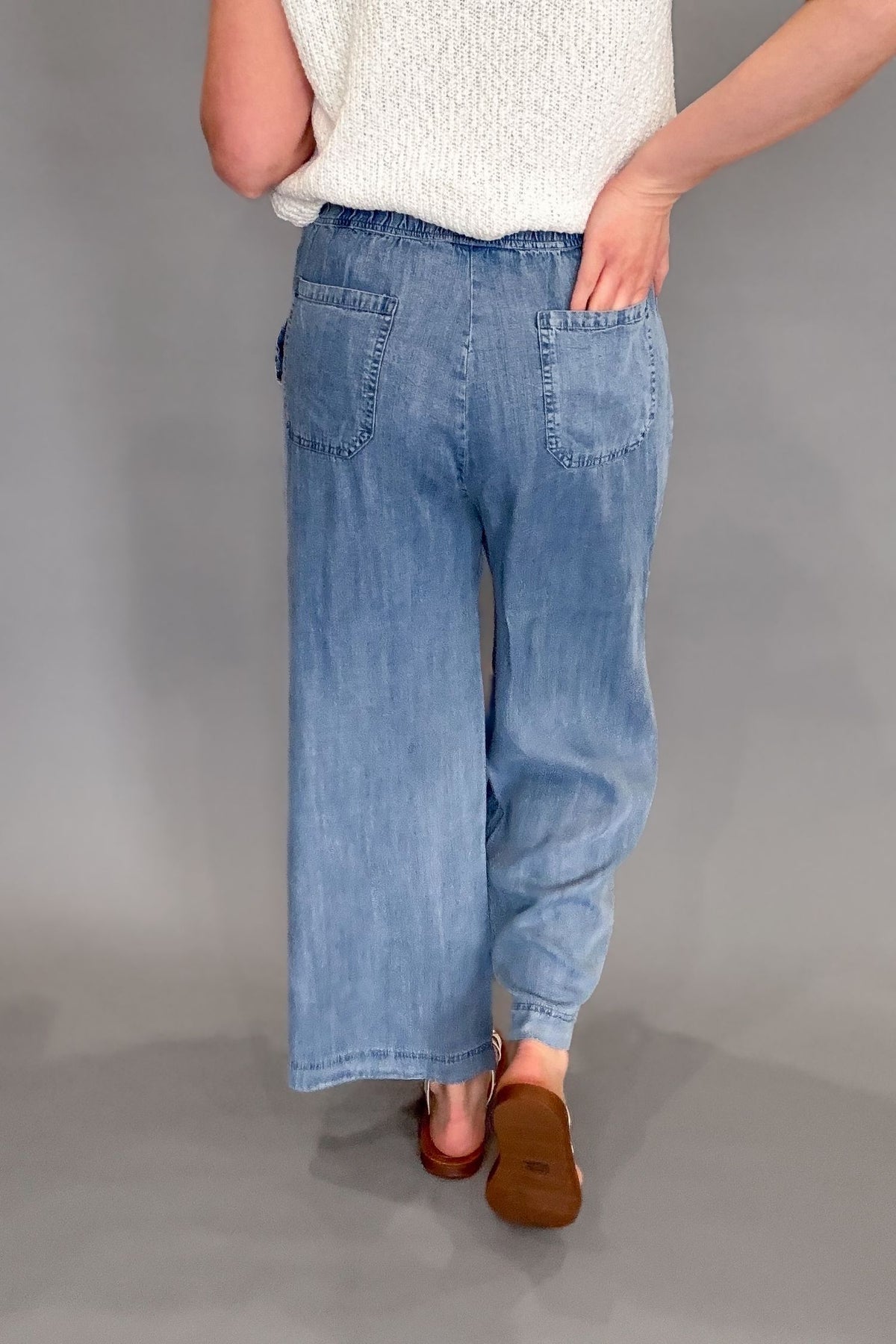 Woman wearing a blue tencel wide leg pant with a white top and sandals showing the back pocket details
