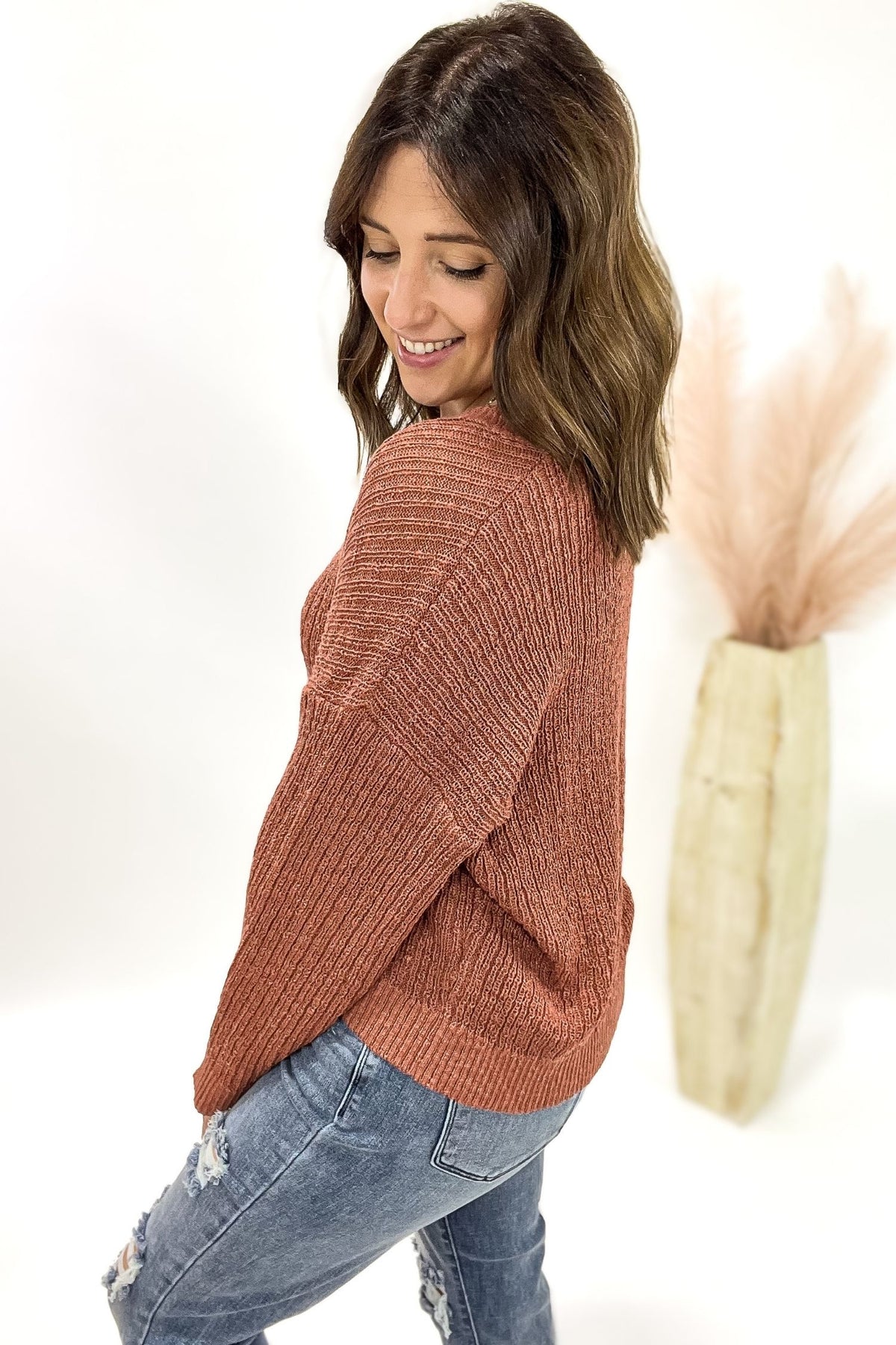Woman wearing a terracotta cardigan with jeans and a white background