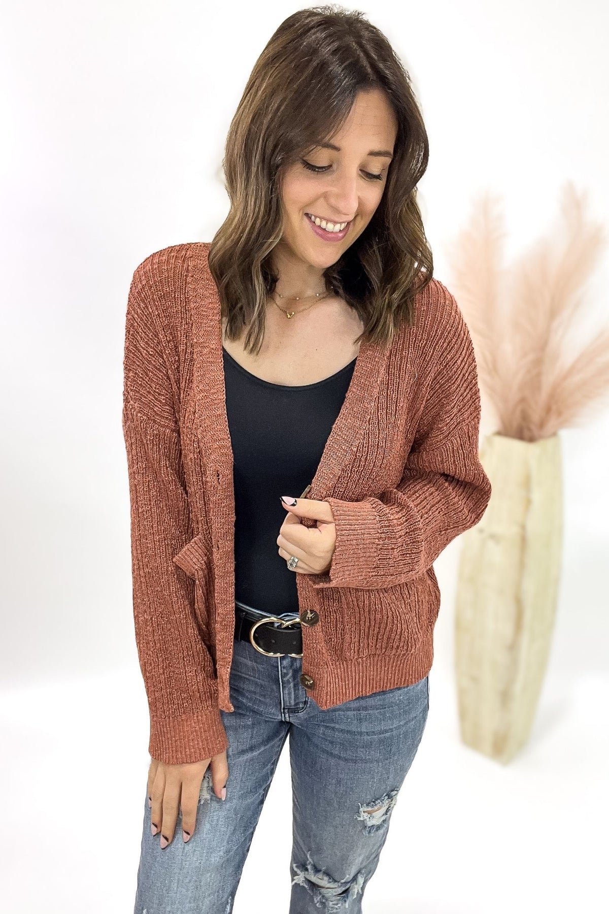 Woman wearing a terracotta cardigan open with jeans and a white background