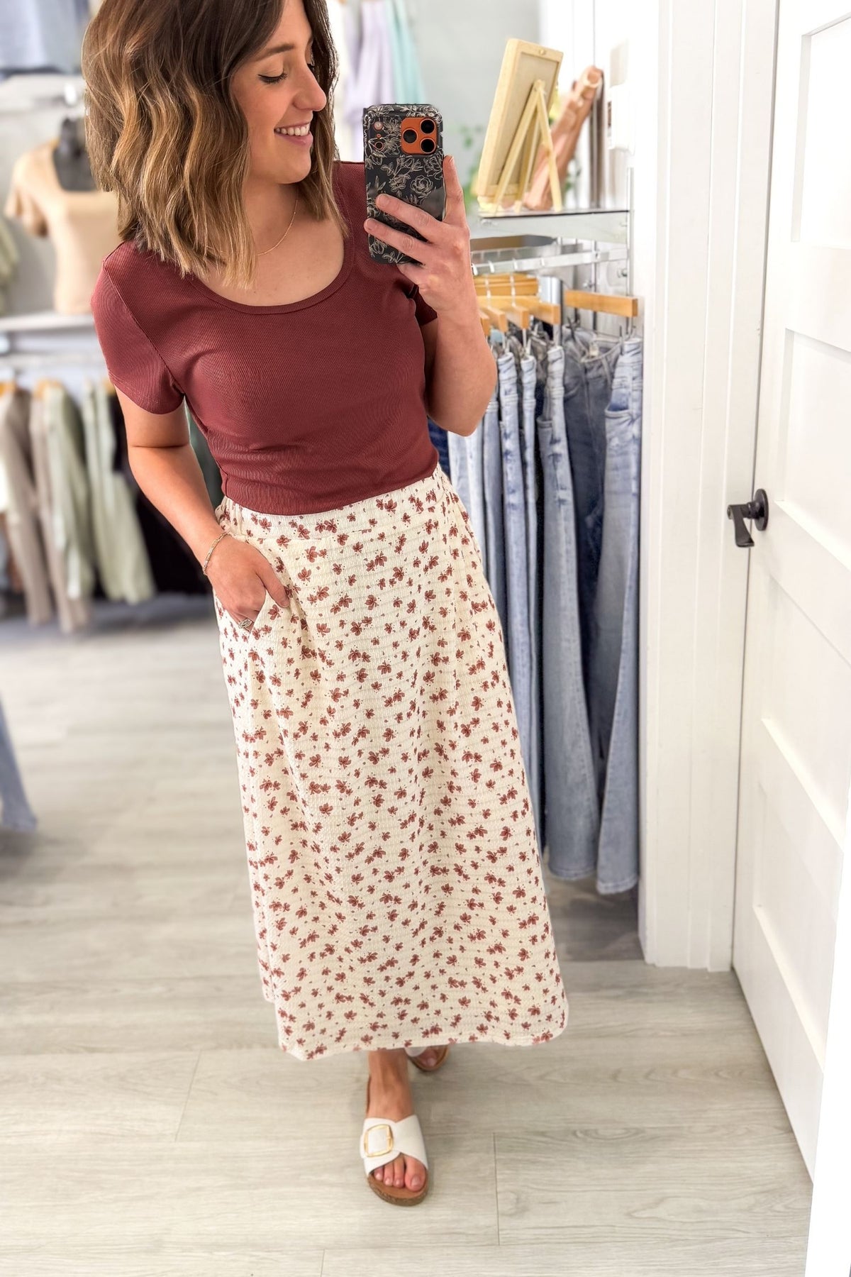 woman taking a selfie wearing a textured floral midi skirt with a garnet colored top in a boutique