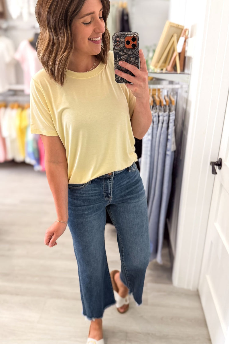 Woman taking a mirror selfie wearing a yellow shirt and blue jeans in a store.