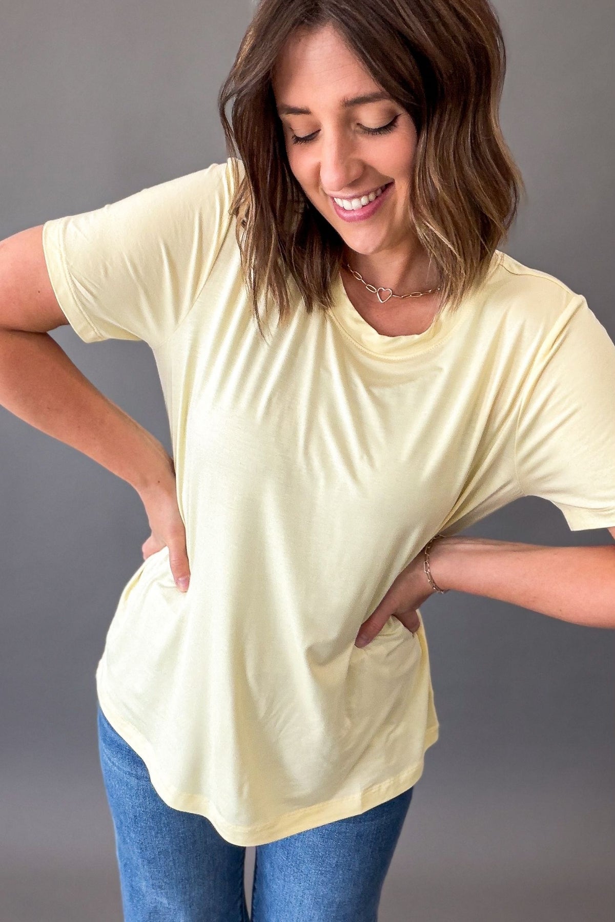 Woman wearing a light yellow t-shirt and blue jeans against a gray background