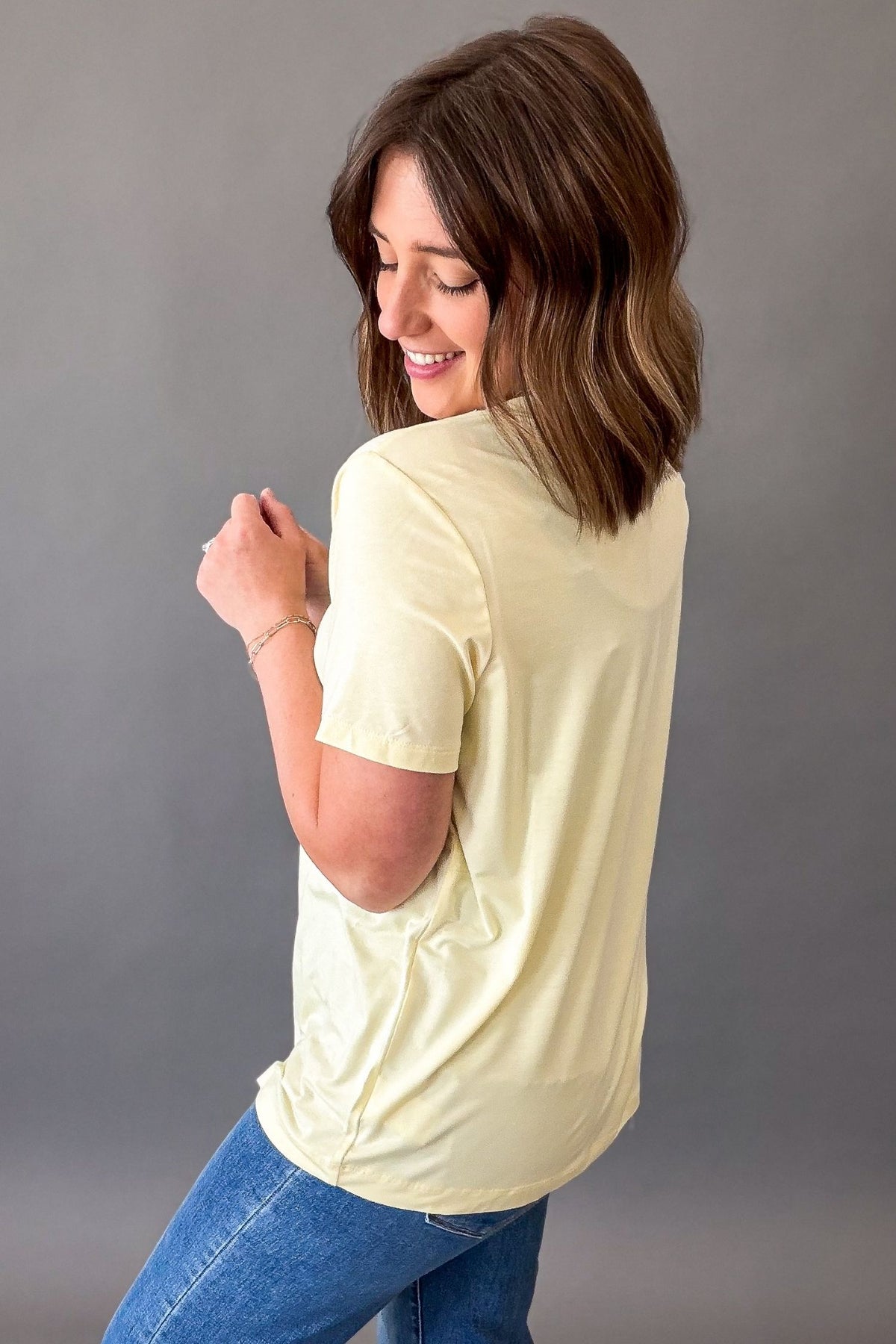 Woman wearing a light yellow t-shirt and blue jeans against a gray background