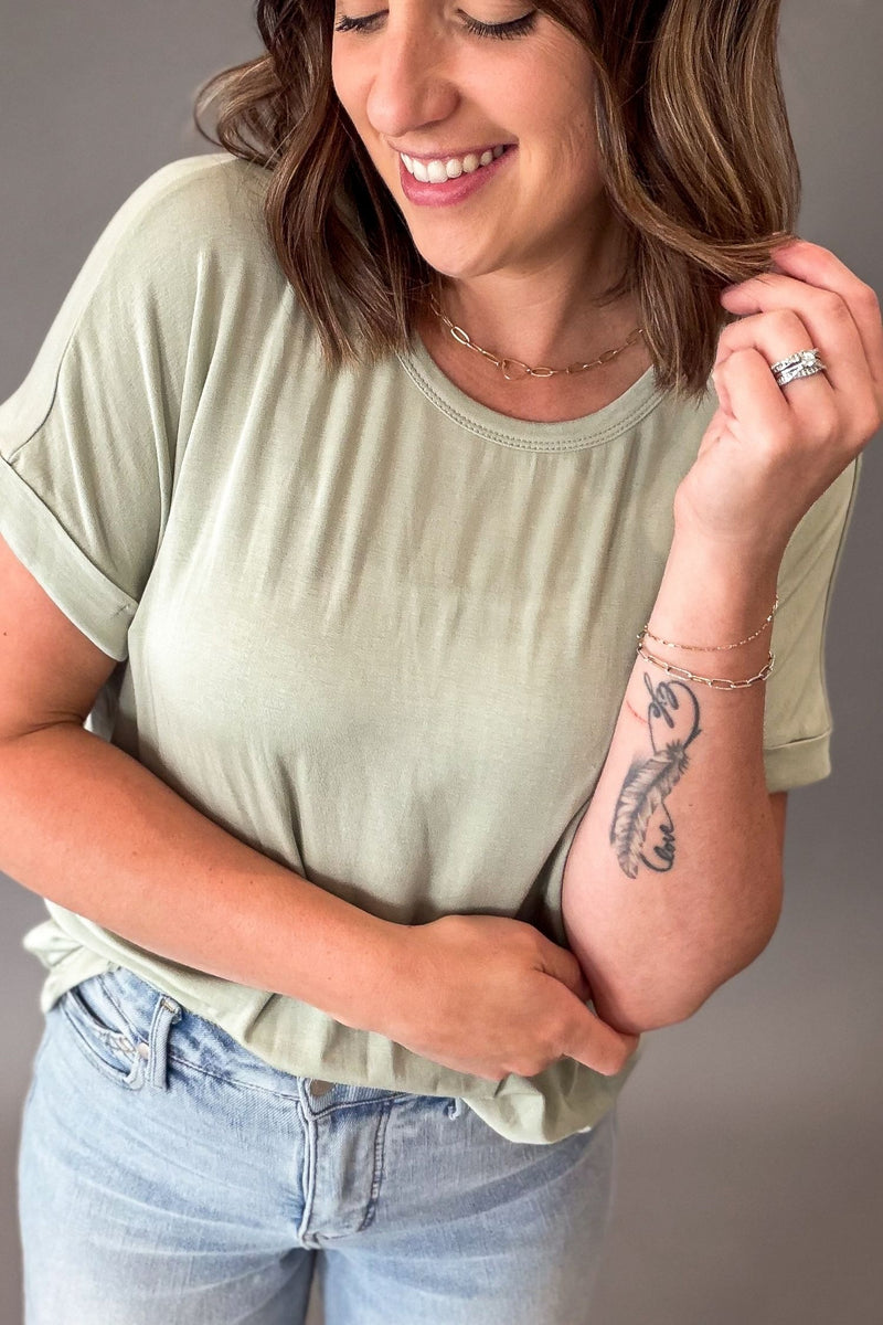 Woman wearing a light green t-shirt and blue jeans with a neutral background