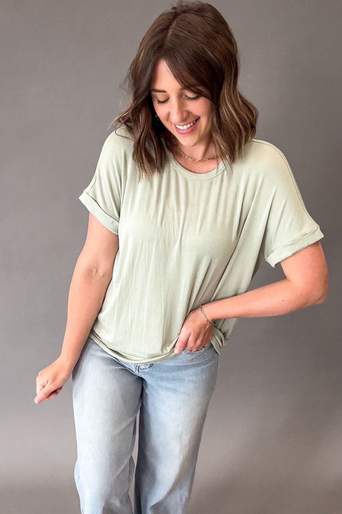 Woman wearing a light green t-shirt and blue jeans against a gray background