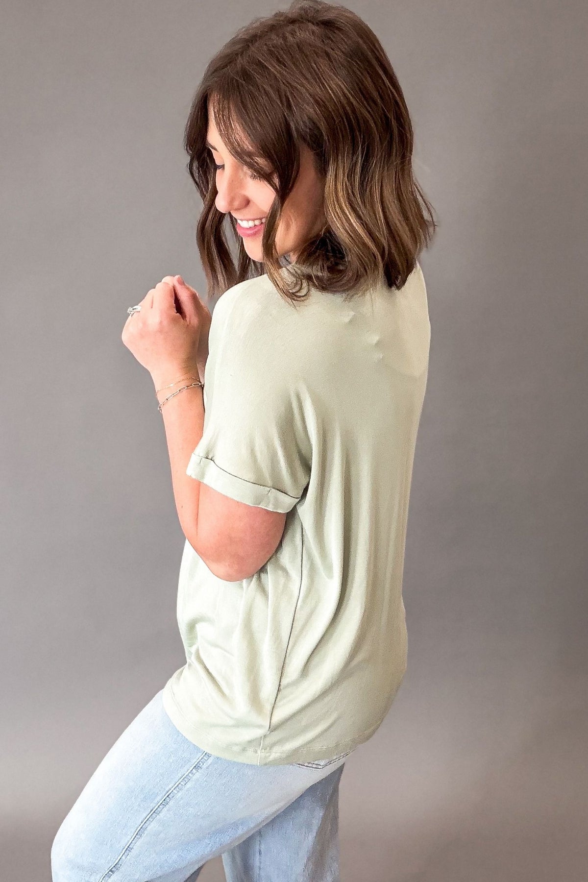 Woman wearing a light green t-shirt and light blue jeans against a gray background