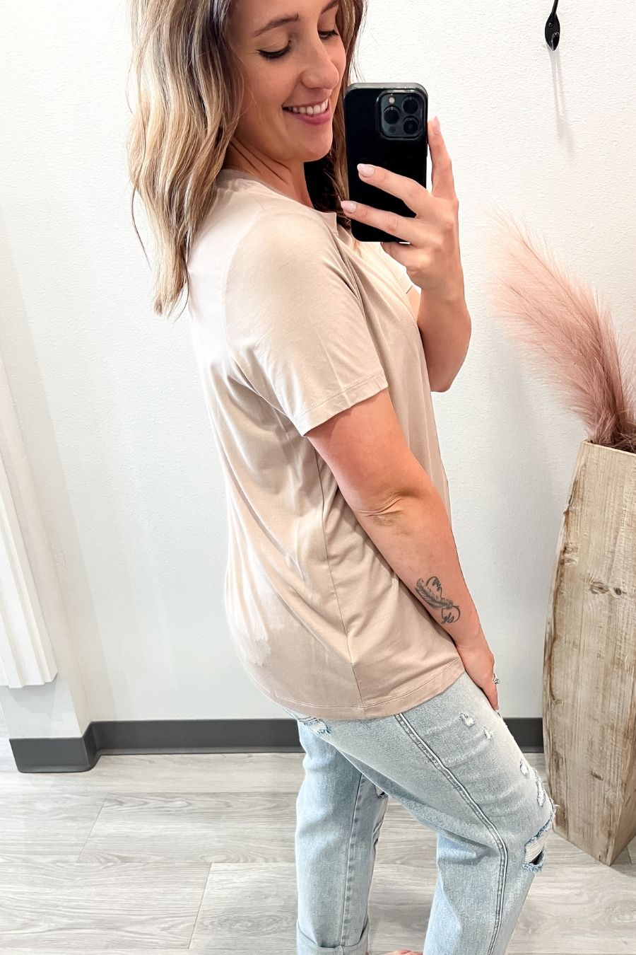 Woman taking a mirror selfie wearing a beige t-shirt and light blue jeans.