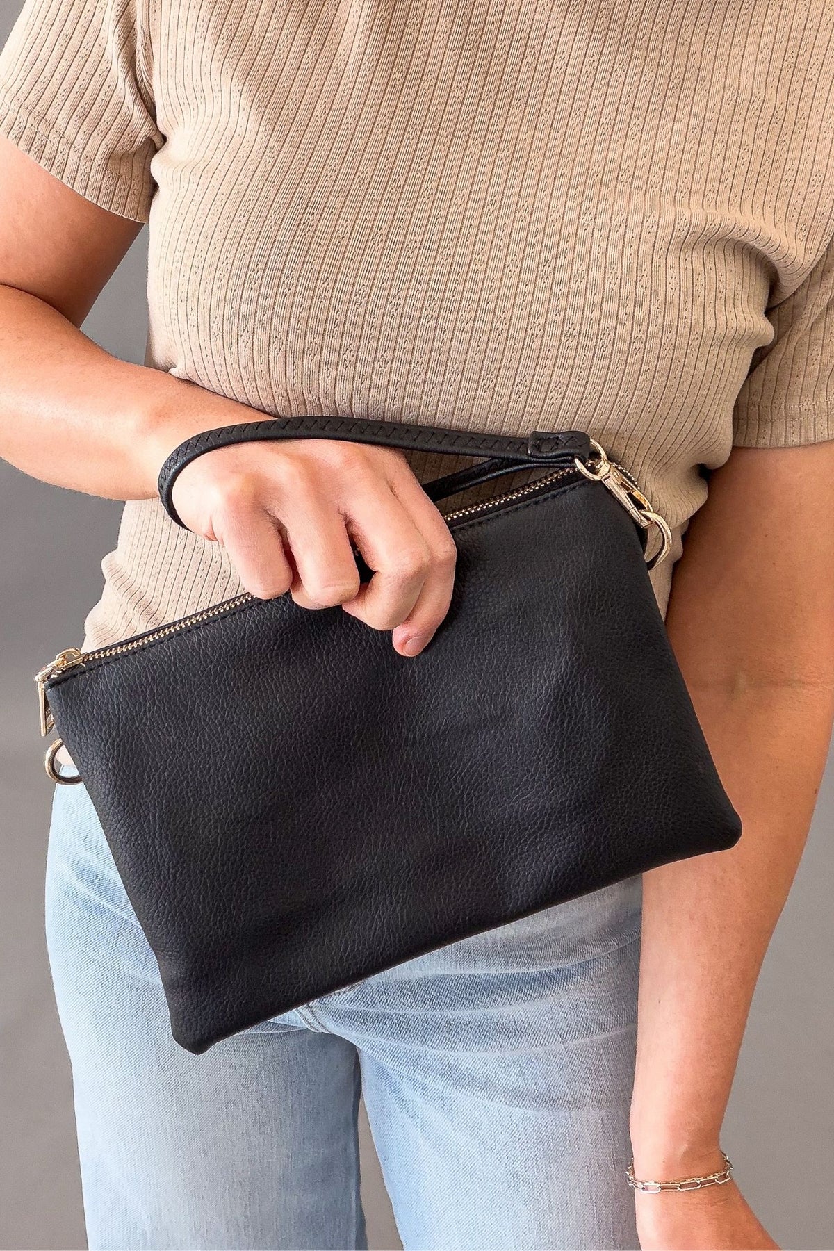 Person holding a black clutch bag with a neutral background